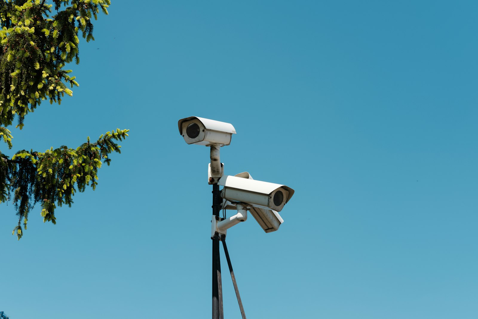 Duas câmeras de segurança instaladas num poste contra o céu azul. Foto: Michał Jakubowski / Unsplash