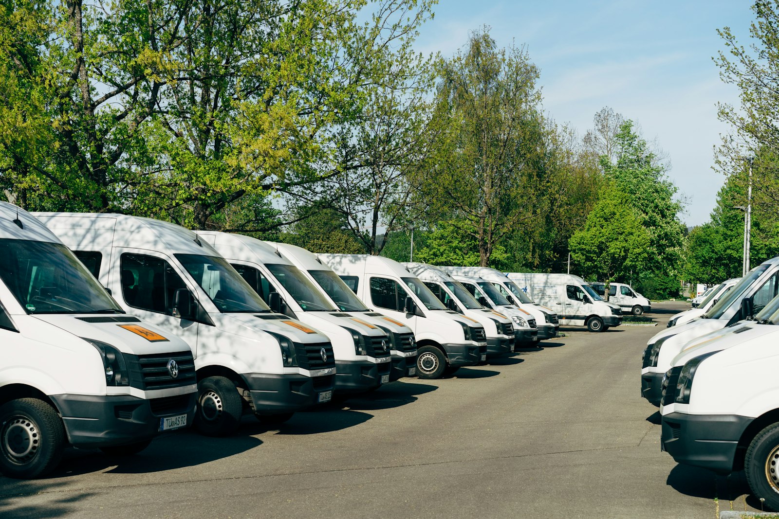 Fileira de vans brancas estacionadas lado a lado num pátio. Foto: Markus Winkler / Unsplash