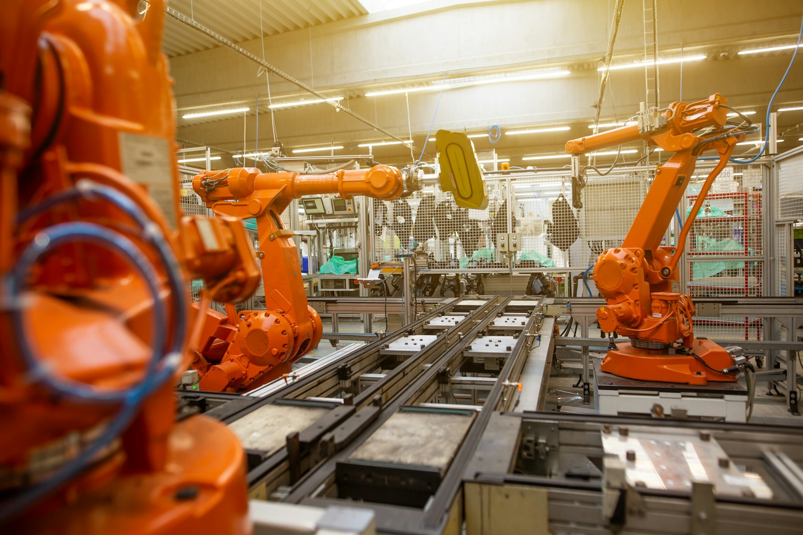 Braços robóticos laranja numa linha de montagem industrial. Foto: Simon Kadula / Unsplash