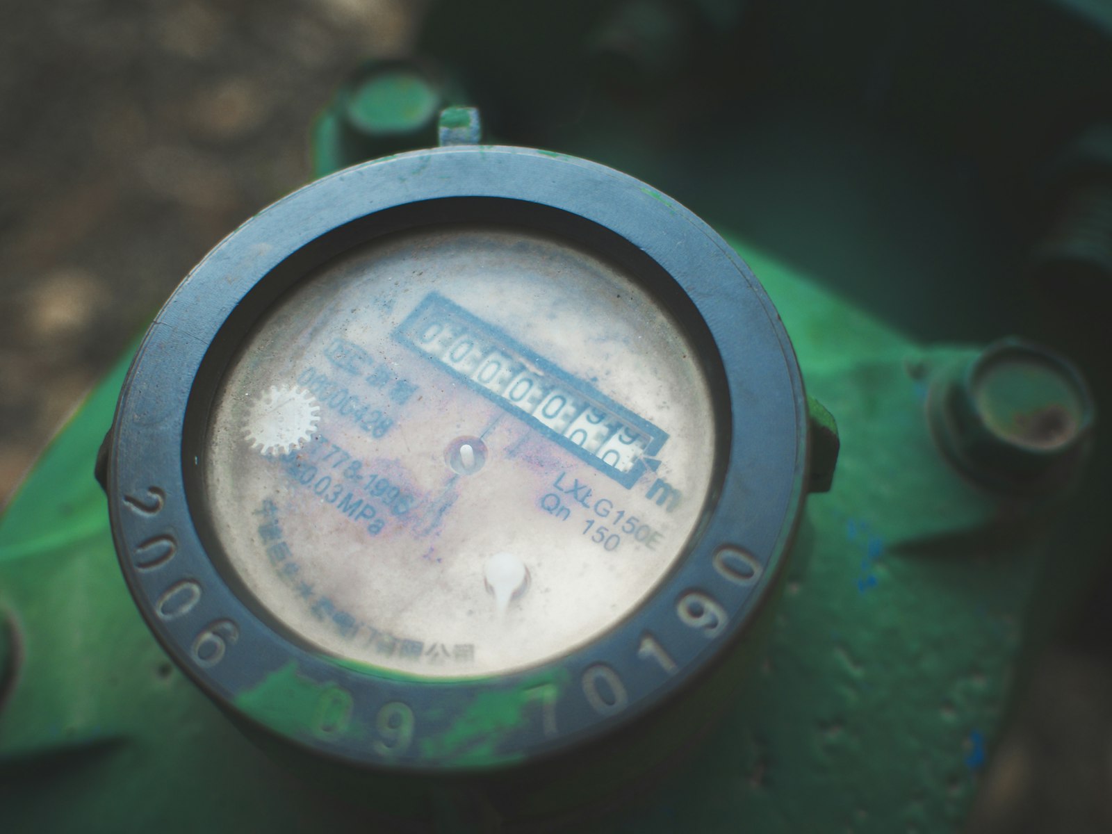 Close-up de um hidrômetro analógico instalado numa tubulação verde. Foto: Hansong Huang / Unsplash