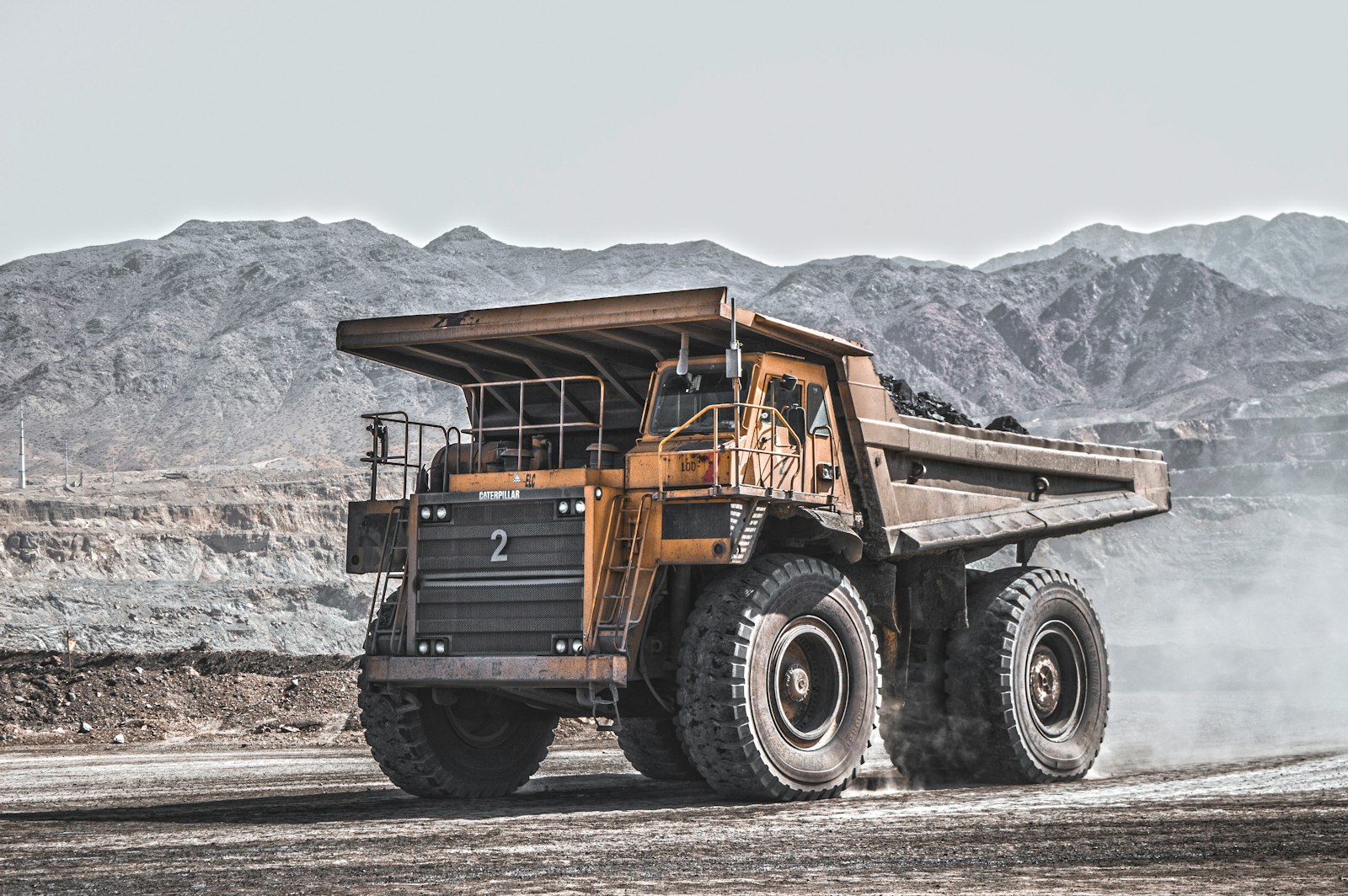 Caminhão fora-de-estrada de mineração em movimento numa cava, com serras ao fundo. Foto: Omid Roshan / Unsplash